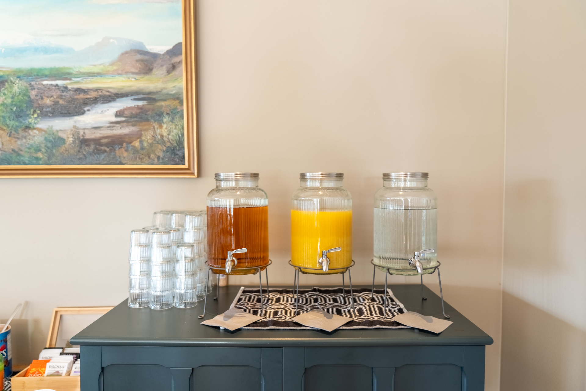 Glass dispensers of juice, iced tea and water on a teal sideboard