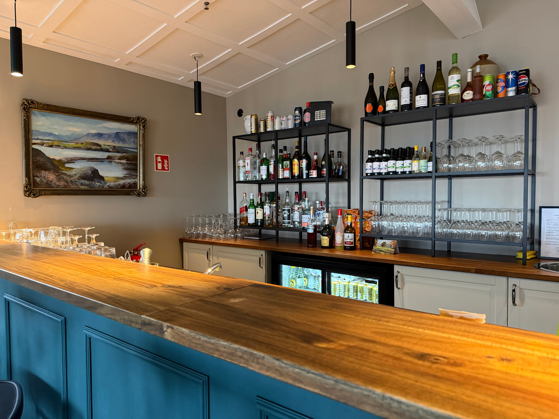 Teal bar with wooden top, shelves of wines and spirits and a framed painting
